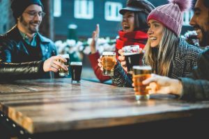Young people having fun drinking beer at bar restaurant - Soft focus on right girl hand holding glass