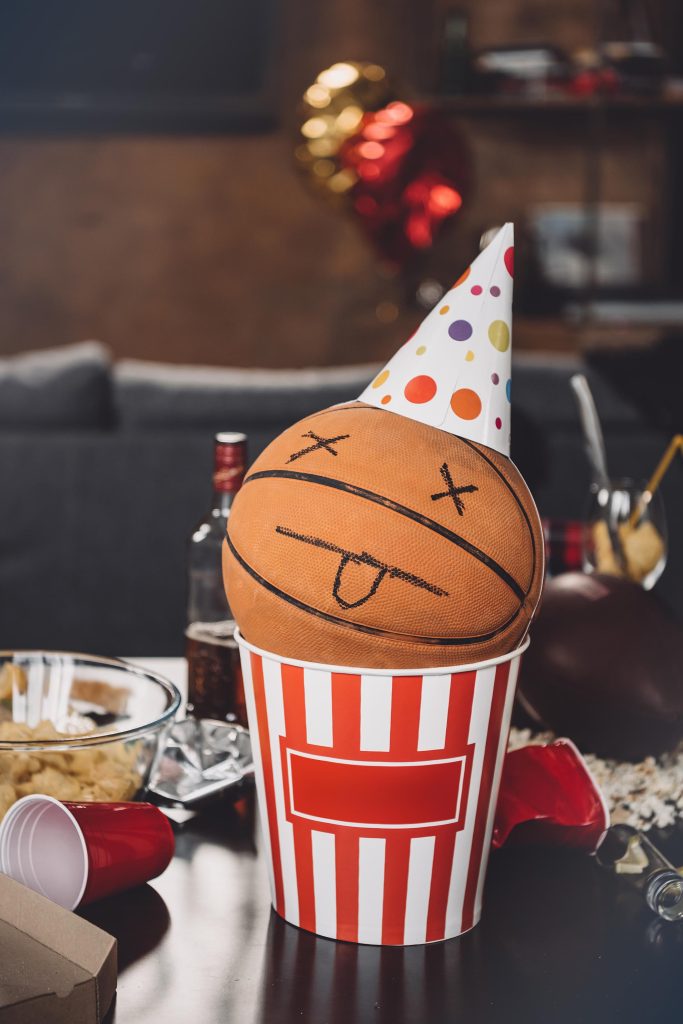 Close-up view of basketball ball with funny face in popcorn box and messy table after party