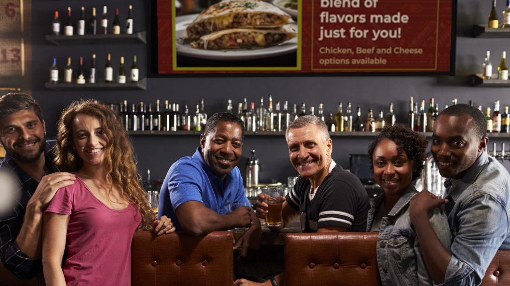 Some individuals at the bar with didigtal signage behind them