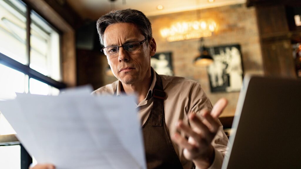 Mid adult cafe owner feeling confused while reading reports after working hours.