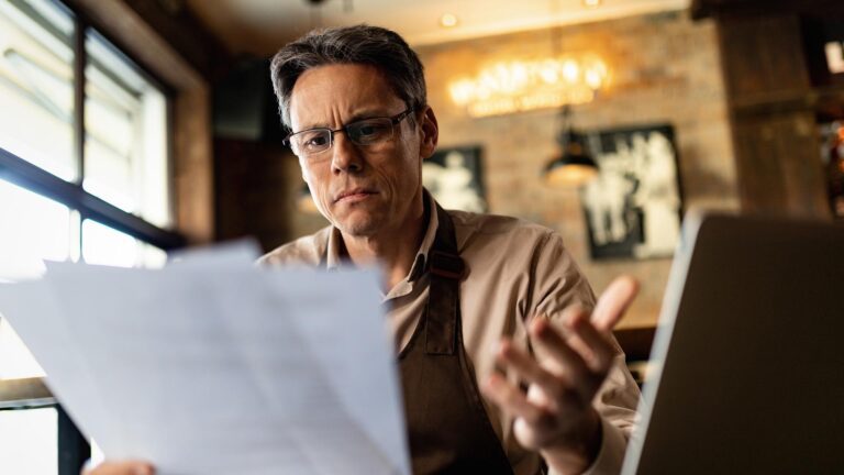 Mid adult cafe owner feeling confused while reading reports after working hours.