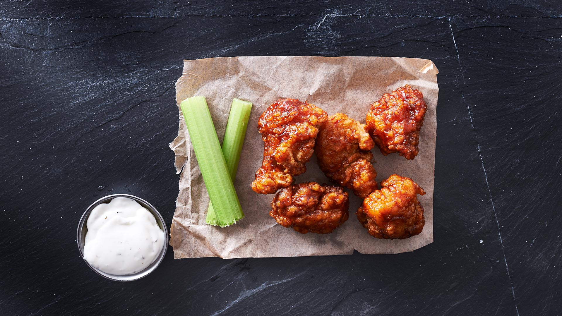bbq chicken hot wings on parchment paper with ranch and celery