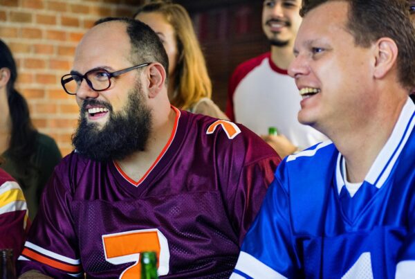 Two friends wearing football jerseys cheering during a football game