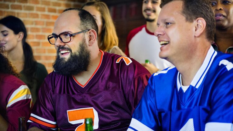 Two friends wearing football jerseys cheering during a football game