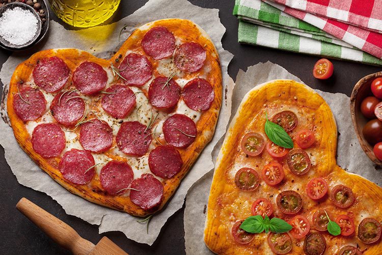 Heart shaped pizza with pepperoni, tomatoes and mozzarella. Valentines day greeting card. Top view