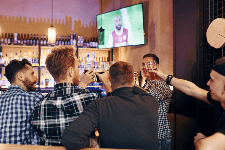 Men cheers at a bar with football on in the background