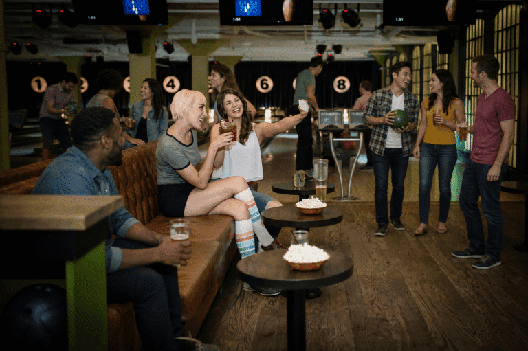 Friends socializing with drinks and bowling balls in a modern bowling alley lounge