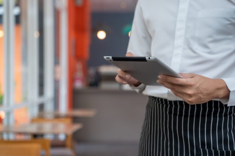 Restaurant staff member holding a tablet beside dining tables